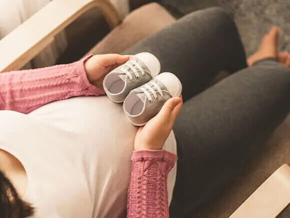 Una mujer embarazada sosteniendo calzados de bebe