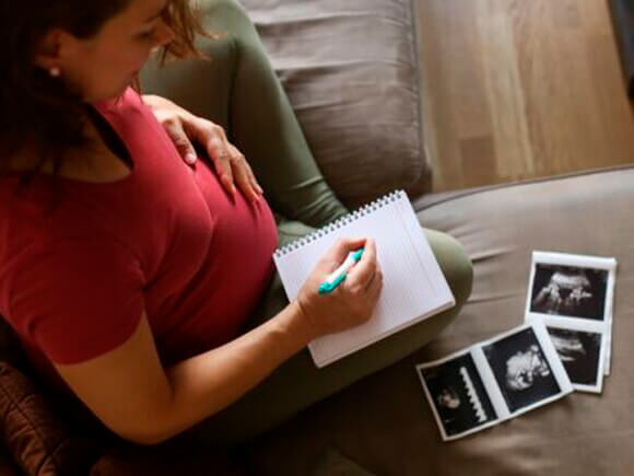 Mamá con un cuaderno mirando la ecografía de su embarazo múltiple.