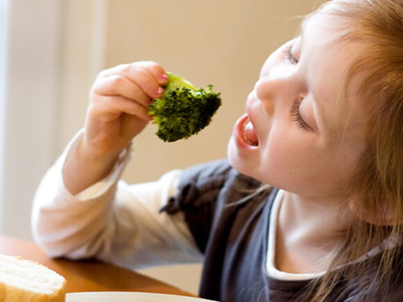 Una niña alimentándose con un brócoli.  