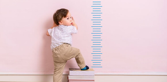 Niño impulsándose en libros para ser medido en la curva de crecimiento y desarrollo.